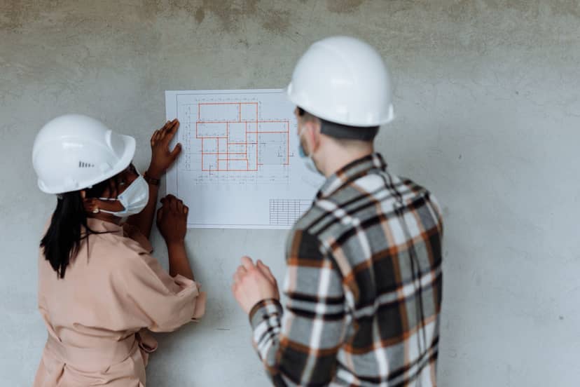 Two engineers in hard hats reviewing a building blueprint on site